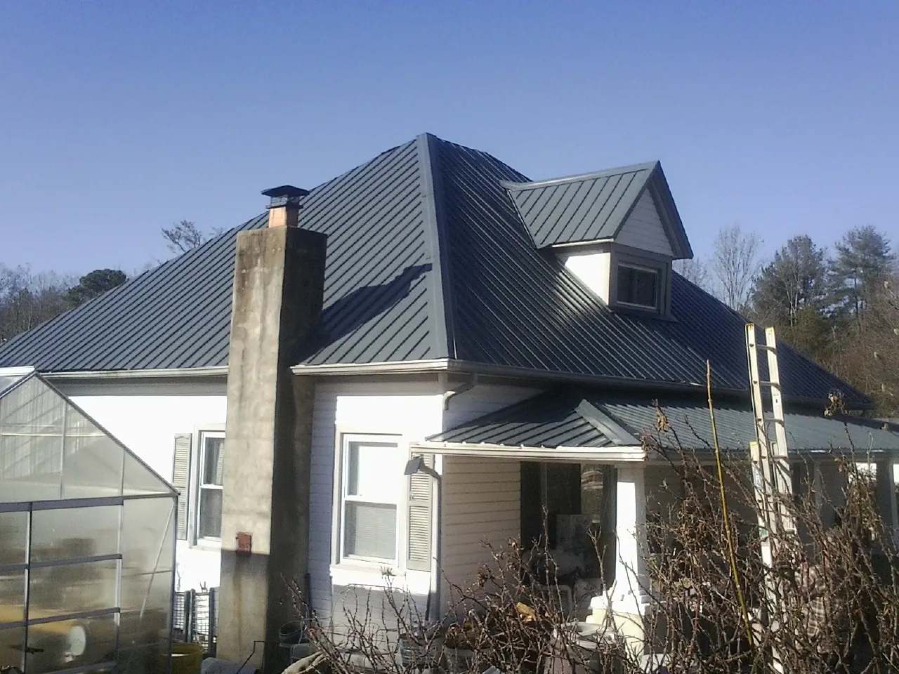 Dark blue standing seam metal roof on a white farmhouse with dormer — Slate & Tile Roof Repair by Roofing Brothers in Black Earth