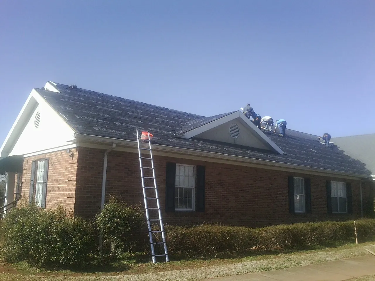 Crew tearing shingles off a brick ranch roof with a ladder set — Metal Roof Repair work by our crew in Black Earth