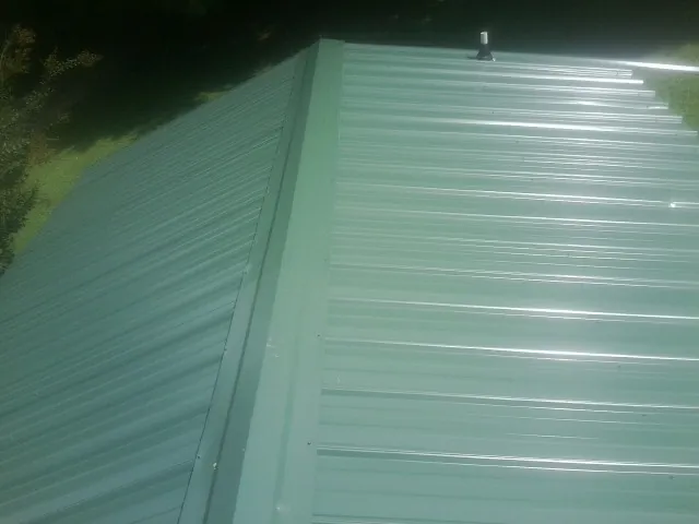 New green metal panels meeting at the ridge of a roof — Flat Roof Repair work by our crew in Black Earth