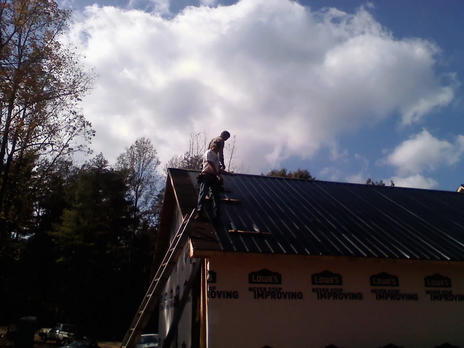 Roofer fastening dark metal panels high against a cloudy sky, from a Roof Inspection job in Black Earth
