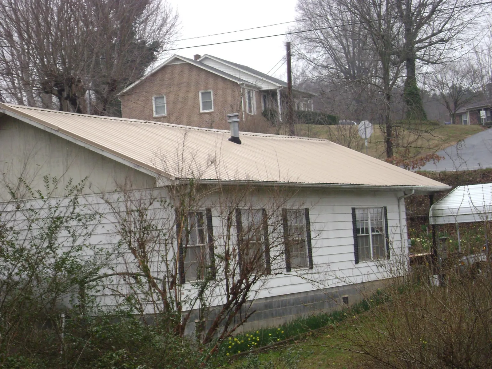 Tan metal roof on a white sided house set into a hillside — Commercial Roofing by Roofing Brothers in Black Earth
